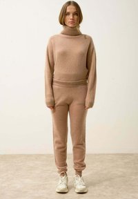 Beżowy sweter z golfem wykonany z dzianiny oraz dopasowane joggery, z prążkowanymi mankietami i pasem, wykonane z miękkiego, teksturowanego materiału.