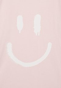 Απαλή ροζ ύφασμα με έναν μεγάλο, υφασμάτινο λευκό χαρούμενο πρόσωπο σχέδιο, που διαθέτει δύο ανυψωμένες καμπύλες για μάτια και ένα πλατύ στόμα.