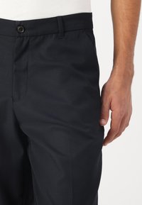 Dark navy trousers made of smooth fabric, featuring a button closure and side pockets, with a tailored fit and neat pleats.