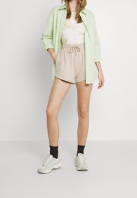 Chemise vert clair surdimensionnée, short beige à cordon de serrage et baskets vert menthe avec chaussettes foncées. Tissu doux, coupe décontractée, style casual.