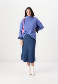 Violet neulekaulusviitta, siniset farkku-midi-hameet, joissa on chevron-saumat, valkoiset nilkkurit ja vaaleanpunainen käsilaukku.