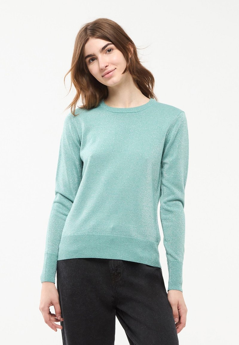 Maglione verde teal chiaro con collo a giro, maniche lunghe e finitura testurizzata. Presenta polsini e orlo a coste. Abbinato a jeans scuri.