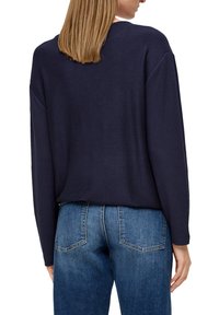 Navyfarbener gerippter Pullover mit lässigem Schnitt, langen Ärmeln und Rundhalsausschnitt, kombiniert mit blauen Jeans.