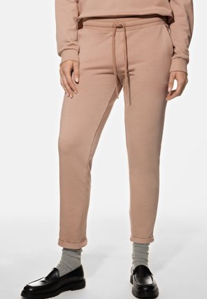 Light pink sweatpants made of soft fabric, featuring a drawstring waist, tapered leg design, and cuffed hems, paired with black loafers.