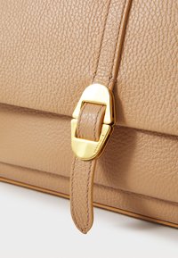 Borsa a tracolla in pelle color tan con superficie texturizzata, accessori in metallo dorato e una tracolla con dettagli a fibbia. Finitura liscia con accenti cuciti.