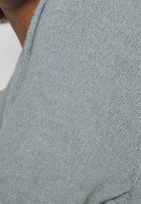 Jasnoszary sweter z dzianiny o miękkiej teksturze i subtelnym wzorze. Materiał wydaje się elastyczny, ma okrągły dekolt i luźny krój.