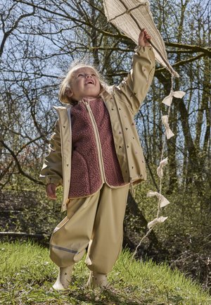 Veste imperméable beige avec motifs en forme de cœur, doublure intérieure en polaire rose, pantalon beige assorti et bottes en caoutchouc, en plein air avec un cerf-volant.
