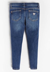 Jeans de mezclilla azul con dos bolsillos traseros, uno de ellos con un parche de marca en forma triangular, sobre un fondo blanco liso.