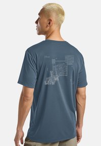 T-shirt blu a maniche corte con stampa grafica raffigurante montagne e coordinate bianche sul retro. Tessuto morbido e leggero.