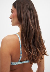Haut de bikini fleuri avec une base bleu clair et des motifs floraux bleus, bretelles réglables et fermeture à clip. Matériau texturé et doux.