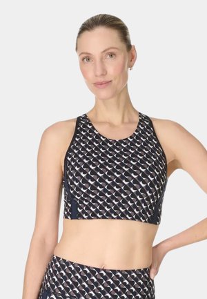 Vrouw met een lichte huid en haar naar achteren gebonden draagt een zwart-witte sportbeha met geometrisch patroon en bijpassende legging.