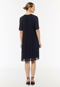 Granatowa sukienka plisowana z krótkimi rękawami i rozszerzanym fasonem. Wykonana z lekkiego materiału o gładkiej teksturze. Szpilki z paskami wokół kostki.