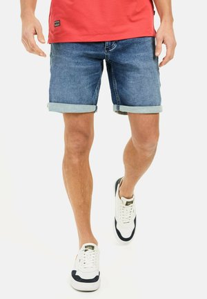 Denim shorts i medium blå med opfoldede kanter, parret med hvide sneakers med marineblå accenter. Stoffet ser holdbart og afslappet ud.