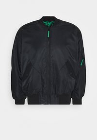 Veste bomber noire avec une finition satinée lisse, poignets côtelés, fermeture éclair à l'avant, poches latérales, et une doublure verte à motifs.
