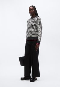 Stickad tröja med svartvitt geometriskt mönster och kontrasterande rosa nederkant. Kombinerad med svarta byxor med vida ben och svarta skor.