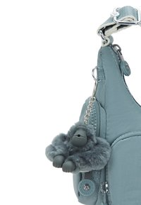 Teal nylon bag featuring a zippered pocket, silver hardware, and a plush gray gorilla keychain for added detail.