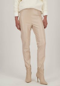 Strakke, hoog getailleerde broek van lichtbeige nepleer. Glad textuur, slanke silhouet, met schuin naaddetails en een glanzende afwerking.
