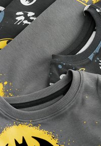 Tre grå sweatshirtar med svarta och gula grafiska mönster, med rund halsringning och varierande tryck, ligger platt för att visa detaljer.