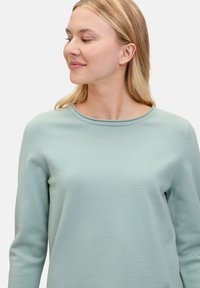 Jasnozielony sweter z okrągłym dekoltem i długimi rękawami, wykonany z miękkiego materiału, z prostym ściegiem wzdłuż brzegów.