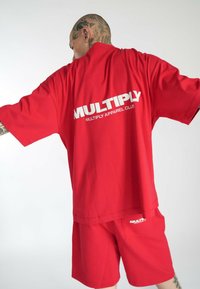 Camiseta oversized roja y pantalones cortos a juego, hechos de una tela suave. Presenta un gran texto de logo blanco en ambas piezas. Diseño simple y moderno.