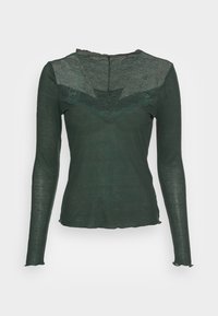 Dlouhý rukáv top v tmavě zelené látce s průhledným krajkovým detailem kolem krku a vlnitým lemem. Hladká textura, přiléhavý střih.