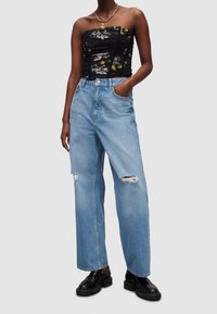 Haut noir sans bretelles avec imprimé floral, associé à un jean large bleu clair déchiré, et des chaussures noires épaisses.