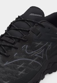 Μαύρο αθλητικό παπούτσι Mizuno με ανώτερο μέρος από διακοσμημένο δίχτυ, μαύρα κορδόνια και μαξιλαρωμένη σόλα σχεδιασμένη για υπαίθριες δραστηριότητες.