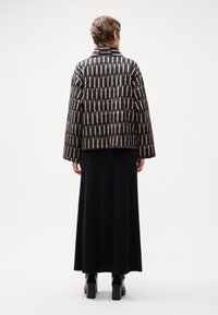 Jacheta matlasată cu bază neagră și modele abstracte bej, având un guler lat și un croi lejer, asociată cu o fustă lungă neagră și botine groase.