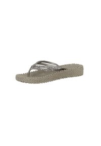 Sandalia de dedo tejida en color beige con una suela texturizada, presenta tiras plateadas brillantes y un diseño minimalista.