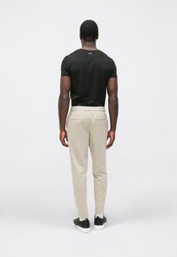 Čierna košeľa s krátkym rukávom a svetlo béžové nohavice s voľným strihom. Topánky sú čierno-biele a majú textúrovaný dizajn.