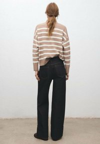 Maglione beige a righe con vestibilità rilassata, abbinato a jeans in denim scuro a vita alta con gambe ampie e cuciture in evidenza.