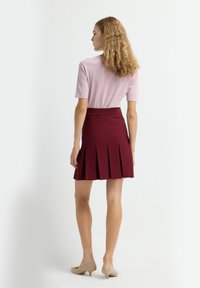 Pruimen plissérok met een aansluitende tailleband, gecombineerd met een lichtroze top met korte mouwen. Model draagt beige hakken, die iets zichtbaar zijn.
