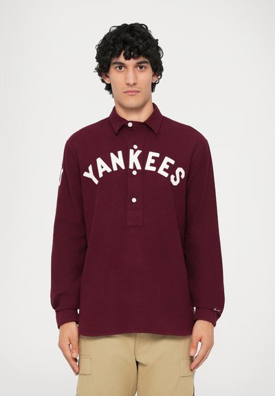 Burgunderfarget langermet skjorte med knapper som har "Yankees" i hvit skrift, krage og forsterket placket. Laget av bomullsblanding.