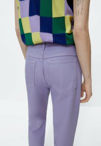 Vaqueros de color púrpura claro con un diseño ajustado, que presentan dos bolsillos traseros y una textura suave. Complementados con una blusa de estampado de tablero de ajedrez colorido.