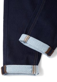 Jean en denim bleu foncé avec les jambes retroussées au niveau des revers montrant un tissu intérieur bleu clair et des coutures marron.