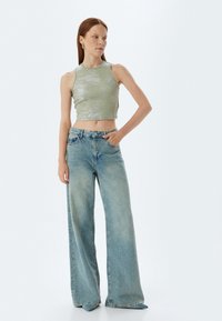 Crop top lucido verde chiaro con silhouette aderente e jeans a gamba larga in blu sbiadito, dotati di design classico a cinque tasche e passanti per cintura.