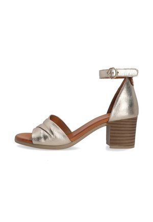 Metallic gold heeled sandal with an open toe, knotted detail on the front, and an ankle strap. Features a textured brown block heel.