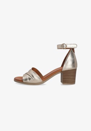 Metallic gold heeled sandal with an open toe, knotted detail on the front, and an ankle strap. Features a textured brown block heel.