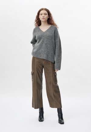 Grijze wollen oversized trui met een V-hals. Gecombineerd met bruine cargobroek met zijzakken en zwarte puntige enkellaarsjes.