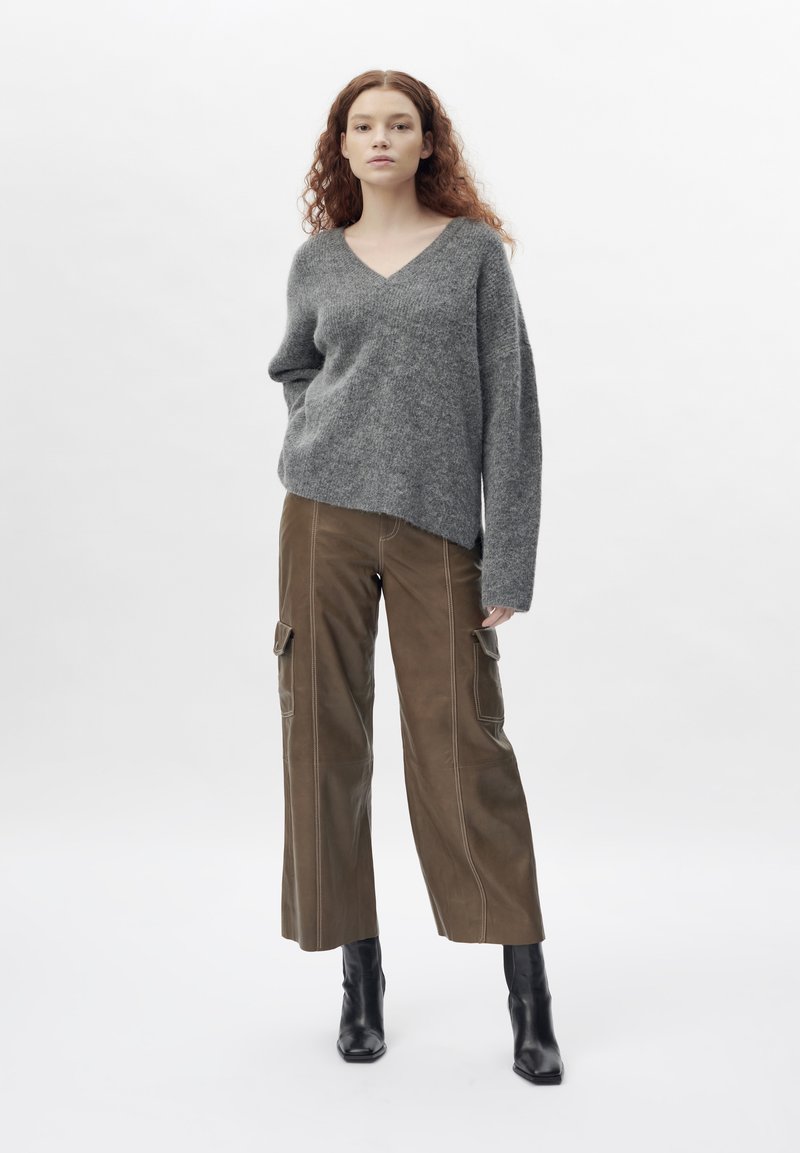 Grauer Wollmix übergroßer Pullover mit V-Ausschnitt. Kombiniert mit braunen Cargo-Hosen mit Seitentaschen und schwarzen spitzen Ankle Boots.
