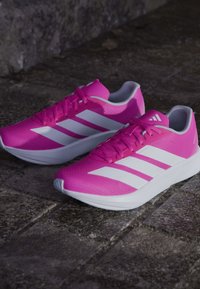 Baskets de sport roses avec une tige texturée et des accents blancs. Comprend trois bandes blanches, un design élégant et une semelle blanche arrondie.