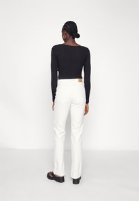 Camisola preta de manga longa combinada com jeans brancos de perna reta, apresentando um design ajustado e um tecido texturizado. Sandálias pretas de plataforma completam o visual.