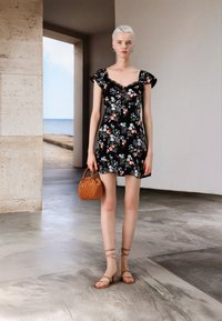 Zwarte bloemenjurk met gerimpelde mouwen, boven de knie lengte, gecombineerd met een geweven bruine handtas en beige sandaaltjes. Gladde textuur.