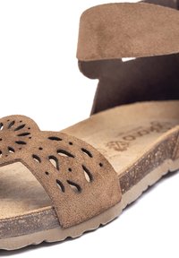 Brauner Wildledersandal mit lasergraviertem Blumenmuster auf den Riemen, Korkfußbett und einer strukturierten Gummisohle für Grip und Komfort.