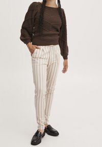 Brun strukturerad tröja med puffärmar, i kombination med krämfärgade randiga byxor med smal passform och svarta loafers, med dragsko i midjan.