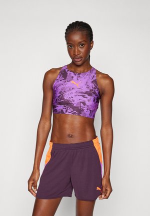 Lilla sports crop top med mønster og orange accenter, parret med mørkelilla shorts med orange sidelapper og logo.