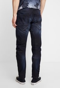 Mörkblå denimjeans med en blekt finish, med bakfickor och slim fit. Matchas med svarta canvas sneakers.