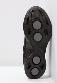 Zwarte atletische schoenzool met een textuur oppervlak, voorzien van ronde en ovale rubberen accenten voor grip. Lichtgewicht, flexibel ontwerp.