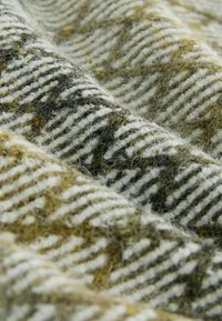 Houndstooth-patterned fabric in earthy tones of green and beige, featuring a soft, textured surface with visible fibers.