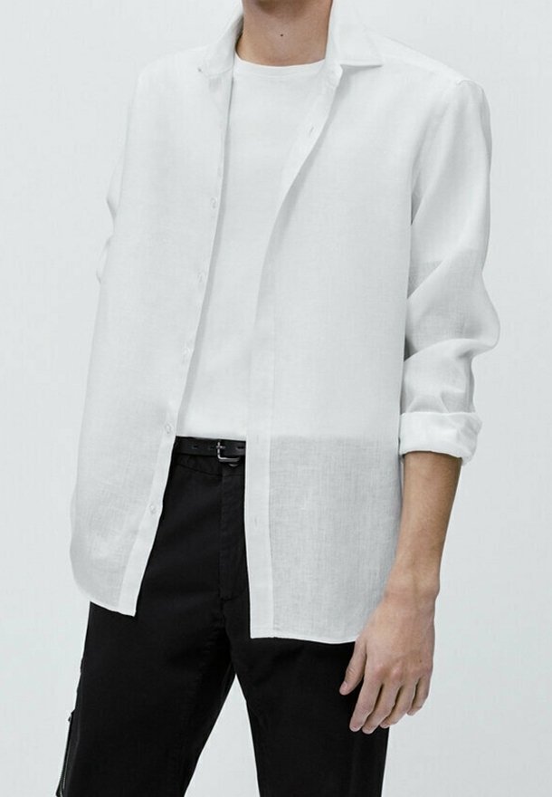 Witte linnen overhemd met lange mouwen, met een knoopsluiting aan de voorkant, open kraag en opgerolde mouwen, gelaagd over een wit t-shirt en zwarte broek.